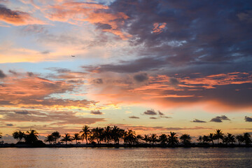 Colorful sunset with silhouettes of palm trees on a tropical island and an airplane high in the sky