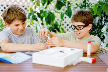 Two kids boys doing chemical experiment in laboratory at school. Children with protective glasses study using pipette dropping liquid to test tube , caucasian , biochemistry . chemistry class.