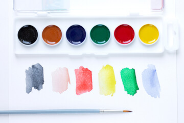 A set of watercolor paints, a paint brush and watercolor color blurs colors on a white background with a copy of the space. Close-up