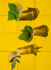 Wall Mural - Refreshing summer drinks in crystal glasses with green leaves yellow tile background with harsh shadows. Sweet cold natural cocktail hot summer day. Non alcoholic soda water mint tonic. Party vacation