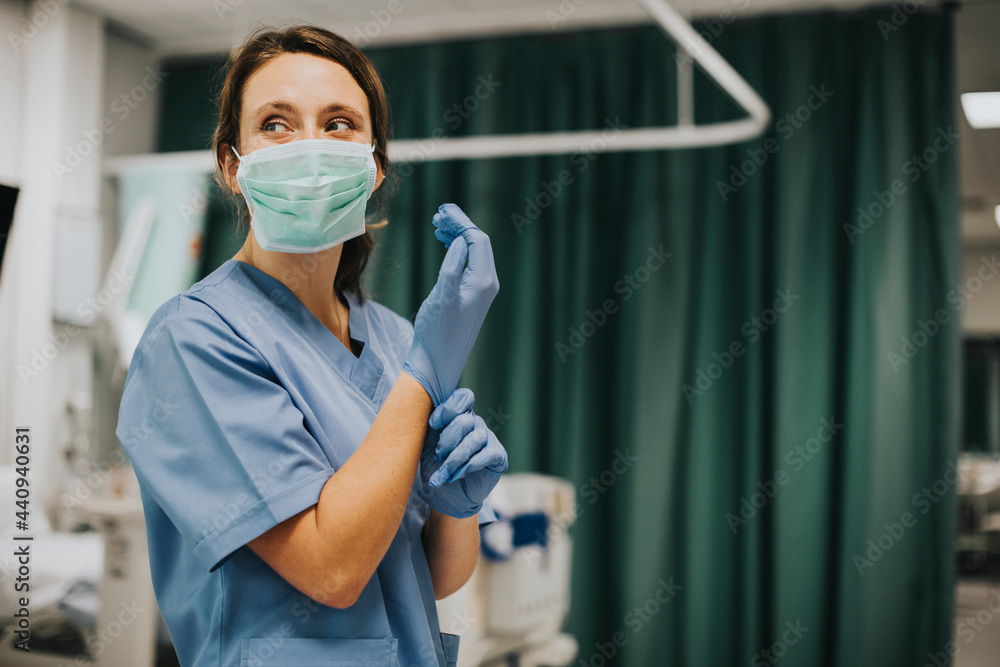 Female nurse with a mask putting on gloves - obrazy, fototapety, plakaty 