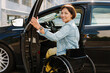© Drobot Dean - Brunette woman in wheelchair getting into car on city street