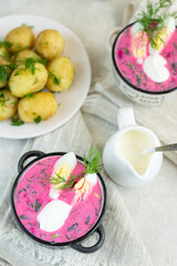 Traditional summer cold soup of beets, herbs, cucumber, eggs and sour cream, on a linen napkin, next to boiled young potatoes. Diet summer menu.