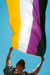 Poster - person outdoors waves a non-binary pride flag