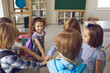 © Studio Romantic - Team of school children joining hands standing in circle in modern classroom. Bunch of cute kids having bonding moment with friends, feeling united and supported. Peer group, community, unity concept