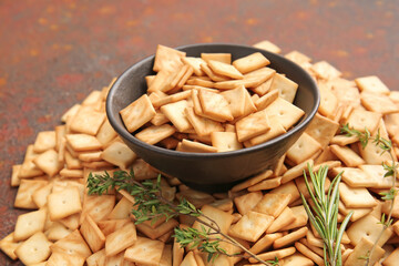 Bowl with tasty crackers on grunge background, closeup