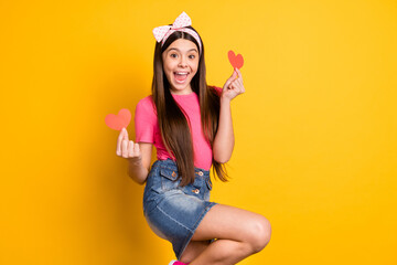 Sticker - Photo of shiny excited small schoolgirl dressed pink t-shirt holding two red paper hearts smiling isolated yellow color background