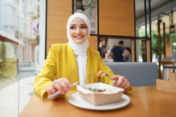 Wall Mural - Young muslim woman in hijab having a lunch in cafe