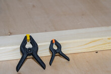 Small Black Plastic Spring Clamps On A Wooden Board And Workbench