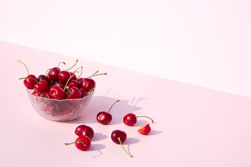 Wall Mural - Glass bowl full of fresh and juicy cherries on a pink and white background. Place for your text. Seasonal summer berries and fruits