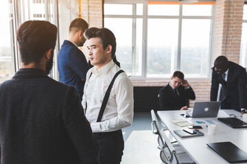 Wall Mural - Mature businessman to discuss information with a younger colleague. People working and communicating while sitting at the office desk together with colleagues sitting.