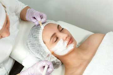 Wall Mural - Facial skin care and protection. A young woman at a beauticians appointment. The specialist applies a cream mask to the face