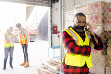Male Warehouse Worker Talking On Smart Phone At Loading Dock