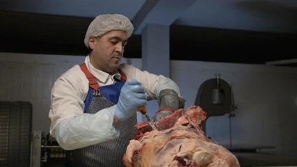 Wall Mural - Butcher cut raw meat with knife at table in slaughterhouse. Male worker prepares fresh meat for delivery to stores.