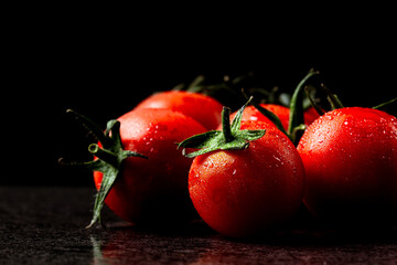 fresh tomatoes with wet and droplet on black stone table and black background