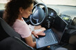 © Taras Grebinets - African-American woman sitting in the driver seat in personal car and working on laptop.