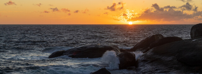 Sticker - Panoramic shot of the seawater and roks under the cloudy sunsets orange light