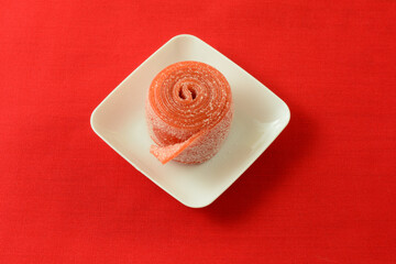 Poster - Sour strawberry fruit roll up candy in white candy dish on red background