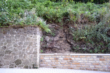 Fragment of a fortress wall and a stone fence. Rock covered with green vegetation