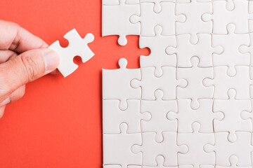 Top view flat lay of hand-holding last piece white paper jigsaw puzzle game last pieces put to place for solve problem complete mission, studio shot on a pink background, quiz calculation concept