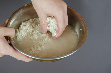 A man washes raw white rice in fresh water. Hands stirring grain