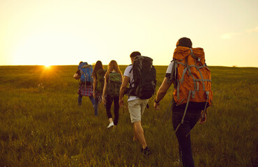 Wall Mural - Five active friends of hikers with colorful backpacks walk through the steppe countryside in summer at sunset. Adventure, travel and tourism concept.