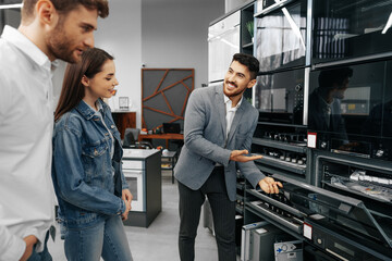 Male shop assistant helps young couple to choose new home appliance