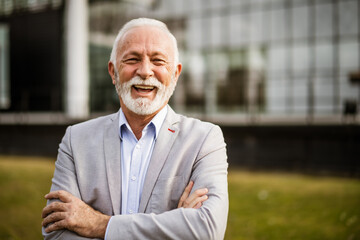 Outdoor portrait of cheerful senior businessman in front of company building.