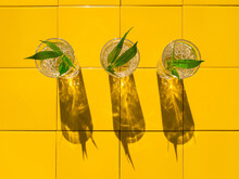 Refreshing Summer Drinks In Crystal Glasses With Green Leaves Yellow Tile Background With Harsh Shadows. Sweet Cold Natural Cocktail Hot Summer Day. Non Alcoholic Soda Water Mint Tonic. Party Vacation