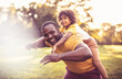 © liderina - Father carrying daughter piggyback. African American father and daughter having fun outdoors.