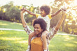 © liderina - African American mother and daughter standing in park. Little girl on mother shoulders.