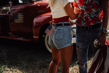 A Couple With Their Vintage Truck - 4th Of July American Independence Day, A Couple Wrapped In A Usa Flag, Sit Together In Preparation For The Fireworks - Happy Young Couple Holding American Flag 