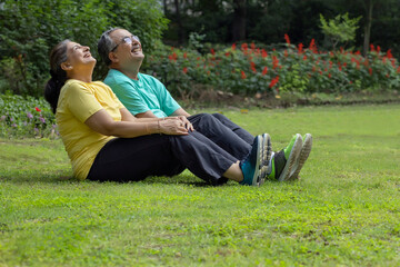 A SENIOR COUPLE SITTING TOGETHER AND LAUGHING WHILE EXERCISING 