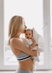 Wall Mural - Young mother holding newborn baby in her arms at home, by the window.