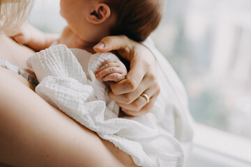 closeup of mother holding newborn baby hand, standing by the window.