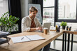 © LIGHTFIELD STUDIOS - smiling young man sitting at desk with paper cup and typing on laptop in modern office