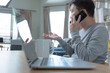 © photobuay - A young businessman use mobile and laptop sitting at wooden table at home, freelancer working on notebook.