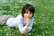 © Anna - Adorable kid boy laying on the grass with daisies flowers in the park in warm summer day. Child dreaming and smiling.