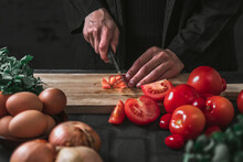 Midsection Of Person Cutting Tomato On Wooden Cutting Board Against Black Background