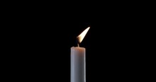 A Single White Candle Burning. The Wind Tries To Put Out The Flame, But It Recovers Each Time. Slow Motion Of Moving Fire Candle Blow By The Wind. Black Background, You Can Use To Overlay An Object.