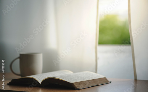 Open the bible with a cup of coffee for reading the Bible or spending time in worship praying to God on a wooden table with window light in the morning