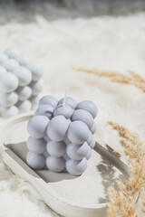 Two grey-blue and white bubble candles on a concrete tray on pastel background, a close up