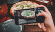 © pavel siamionov - woman hand with smartphone photographing pizza at restaurant or cafe