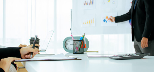 Banner background and selective focus on table with hand writing minute meeting. Blur man presenting working project and showing marketing plan on whiteboard in indoor modern office or workplace.