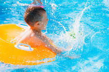 Kid Boy Playing Outdoor Pool Of Resort. In An Inflatable Yellow Circle With A Ball. Children Frolic With Water Toys.