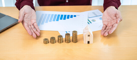 Asian businessman hand protecting house model with coins stack and checking chart financial on paperwork