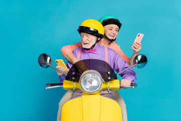 Sticker - Portrait of two cheerful elderly retired pensioner friends riding bike using device gadget app isolated over bright blue color background