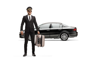 Wall Mural - Full length portrait of a chauffeur with a car in a uniform and sunglasses carrying a suitcase