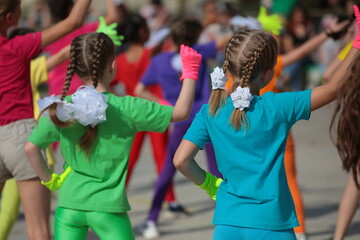 A little girl with long pigtails with many friends in a group at a children's music festival of sports fitness gymnastics.School and preschool physical education.Happy childhood concept. Background