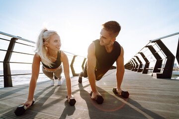 Young fitness couple is doing workout at the beach pier. Young man and woman doing exercises outdoors in the morning. Sport, Active life.